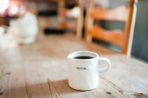 Coffee mug that reads 'begin.' sitting on wood table.  When starting your side hustle, start small, be just start!